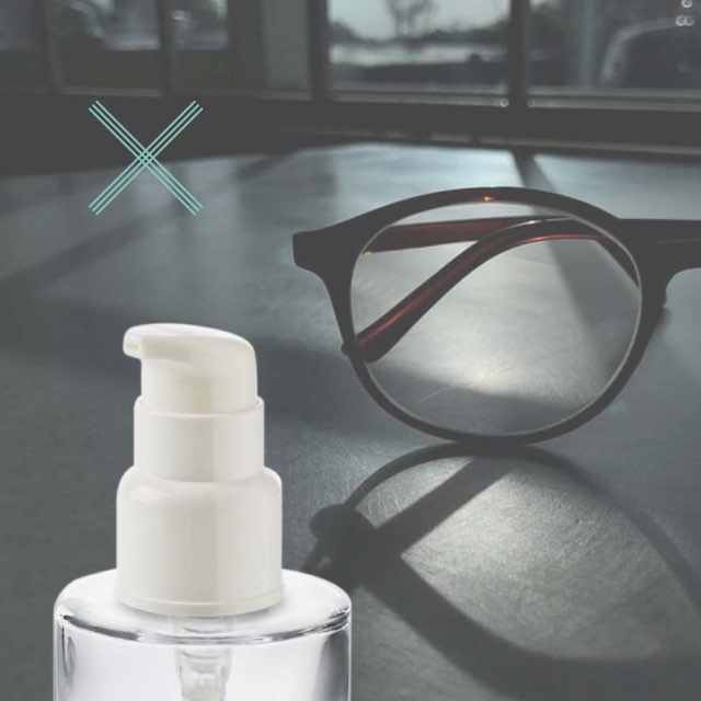 A glass cosmetic bottle with a pump placed on a desk with glasses